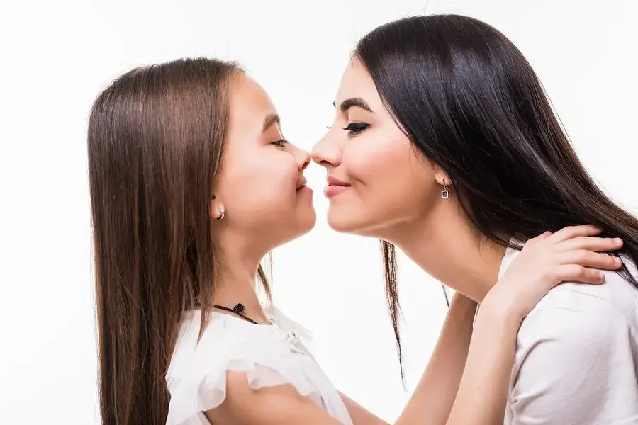 Mother and young daughter touching noses affectionately against a white background.