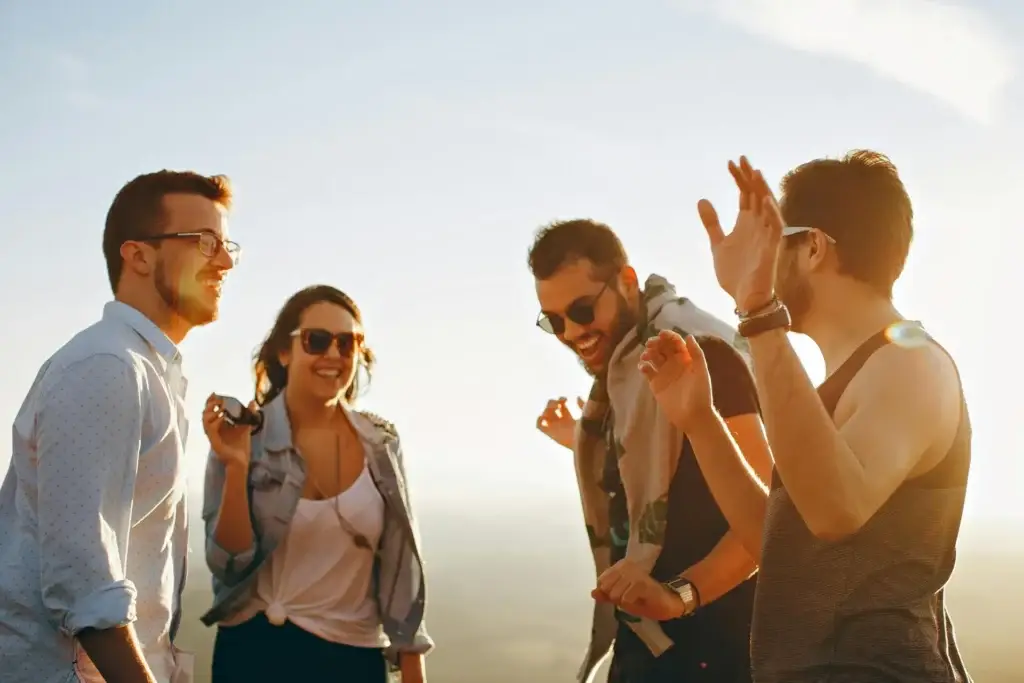 Group of young friends laughing and talking together outdoors at sunset.